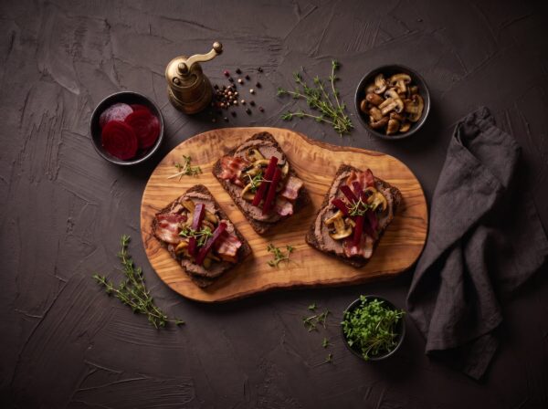 Rugbrødsmadder med varm bisonleverpostej, sprød bacon, svampe og rødbeder på et bræt.