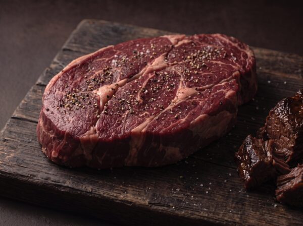 Rå bison tykkam med salt og peber på et mørkt træbræt, med mørt braiseret kød ved siden af.