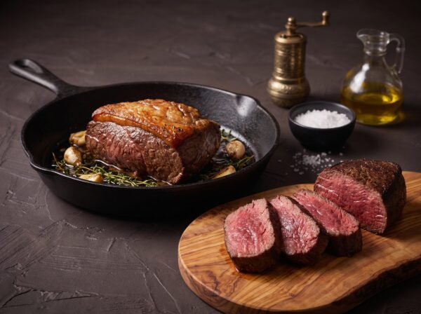 Bison culotte med sprød fedtkappe i en støbejernspande, med tykke skiver på brættet.