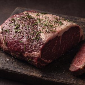 Rå cuvette af bison med salt, peber og rosmarin på et mørkt træbræt, med stegte skiver ved siden af.