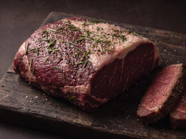 Rå cuvette af bison med salt, peber og rosmarin på et mørkt træbræt, med stegte skiver ved siden af.