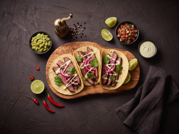 Tacos med grillet flanksteak, syltede rødløg og koriander, med guacamole og salsa ved siden af.