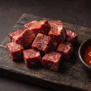 Rå gullaschtern af skotsk højlandskvæg med paprika på et mørkt træbræt, med en skål færdig gullasch ved siden af.