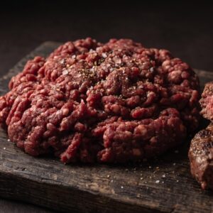 Hakket bisonkød 6-8 % på et mørkt træbræt, med en halveret grillet bisonbøf ved siden af.