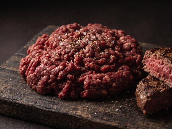 Hakket bisonkød 6-8 % på et mørkt træbræt, med en halveret grillet bisonbøf ved siden af.