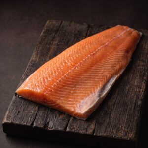 En hel rå laksefilet uden ben med orange kød på et mørkt træbræt.