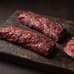 To rå nyretapper (onglet) af skotsk højlandskvæg på et mørkt træbræt, med stegte skiver ved siden af.