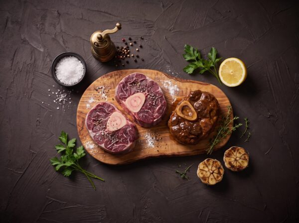 Rå osso buco af bison med marvben på et oliventræsbræt, med et braiseret stykke ved siden af.