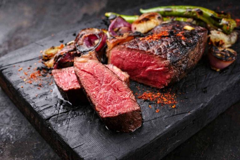 En saftig bøf, stegt medium-rare, skæres ud på et mørkt træbræt og pyntes med grillede løg, grønne peberfrugter og et drys røde krydderier.