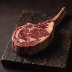 Rå tomahawk steak af skotsk højlandskvæg med det lange ribbensben, fin marmorering og fedtkant, på et mørkt træbræt.